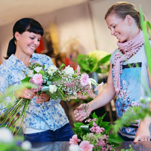 Kaksi naista ihailemassa kukkakimppua, jota toinen pitää käsissään.