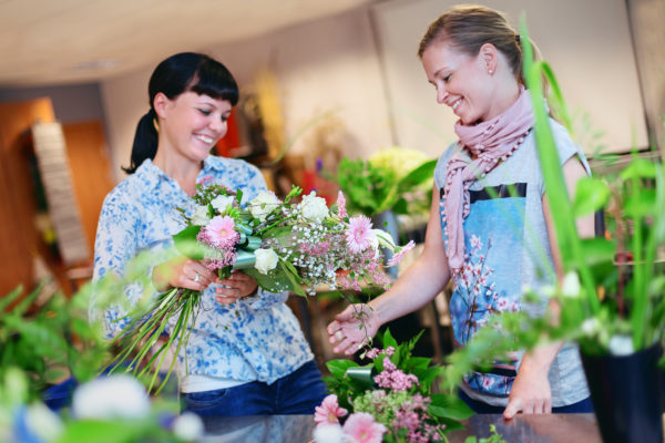 Kaksi naista ihailemassa kukkakimppua, jota toinen pitää käsissään.