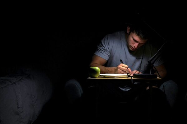 Kuvituskuva: mies kirjoittaa muistikirjaa pimeässä huoneessa.