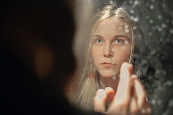 Kuvituskuva: nuori nainen katsoo itseään peilistä tummasävyisessä kuvassa.