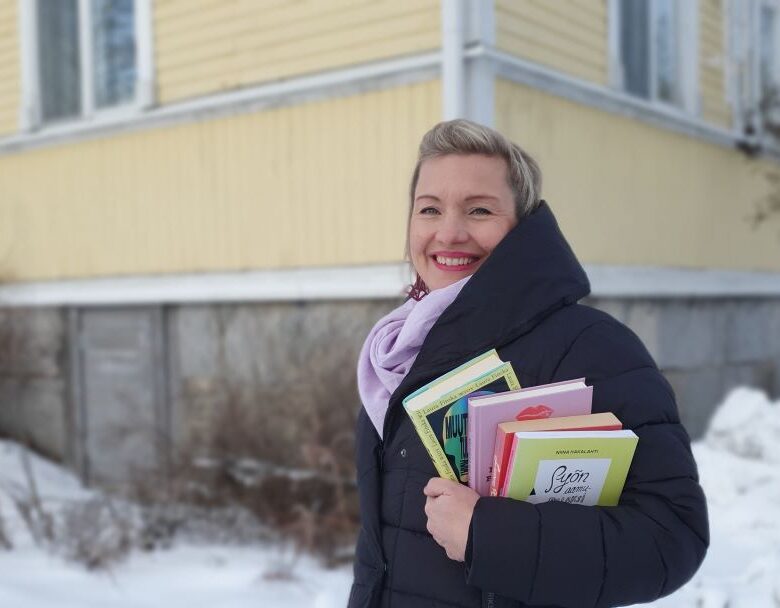 Helena Murtonen-Leppä seisoo hymyillen, kirjoja kädessään keltaisen vanhan puutalon pihalla.