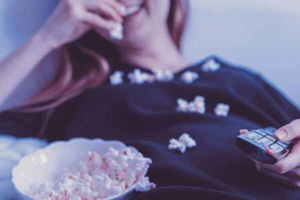 Kuvituskuva: nainen syö popcornia kaukosäädin kädessään.