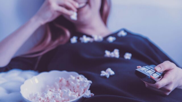 Kuvituskuva: nainen syö popcornia kaukosäädin kädessään.
