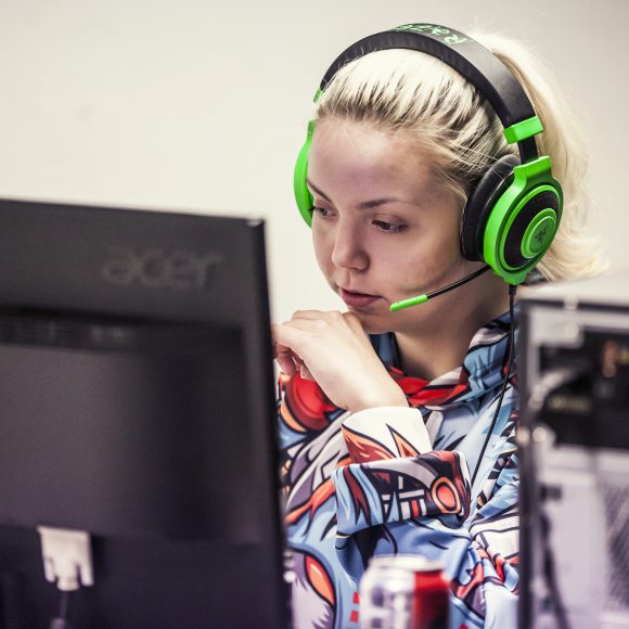 Nainen tietokoneella kuulokkeet päässä.