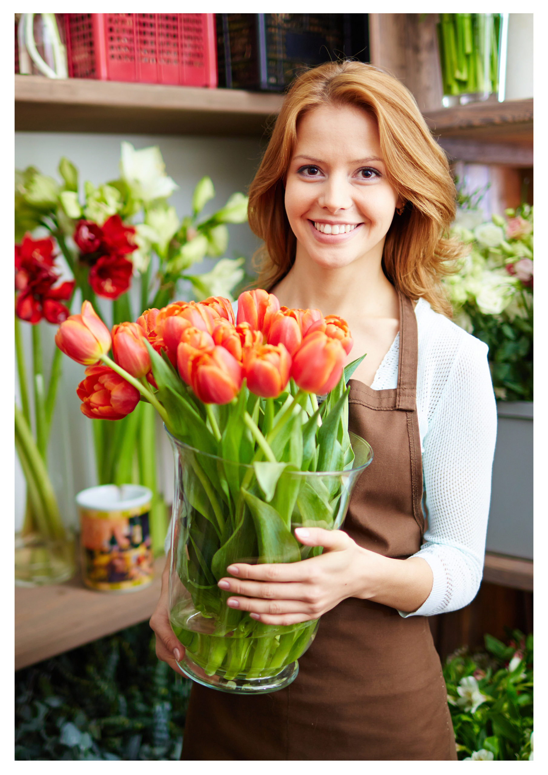 Nainen, jolla on ruskea esiliina pitelee maljakkoa, jossa punaisia tulppaaneita käsissään.