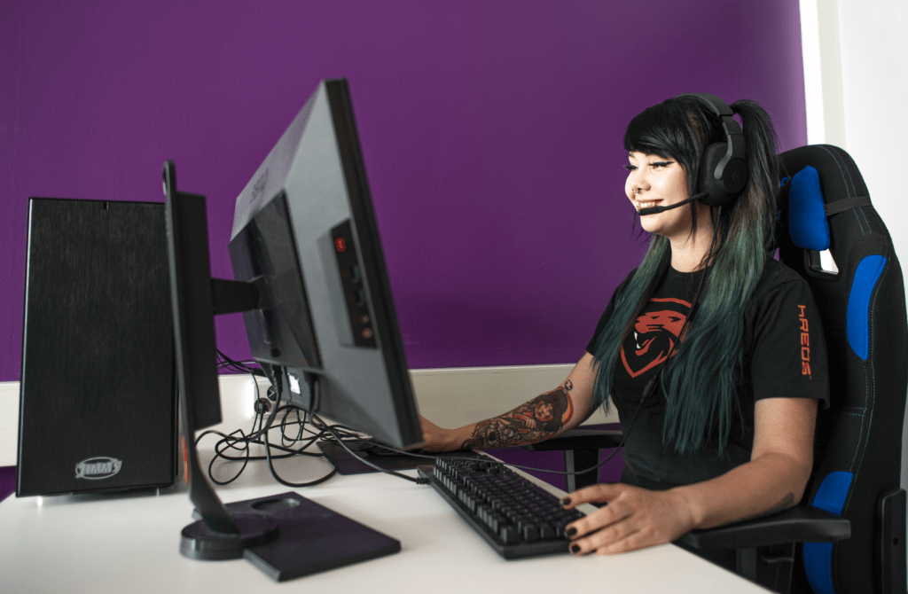 Nainen istuu tietokoneella kuulokkeet päässä ja hymyilee.