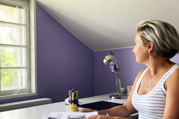 Lyhythiuksinen nainen katsoo ulos ikkunasta talossa, jossa violetit seinät.